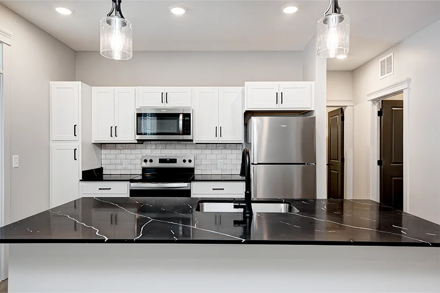 Apartment kitchen with black quartz countertop, white subway tile blacksplash, and stainless steel appliances
